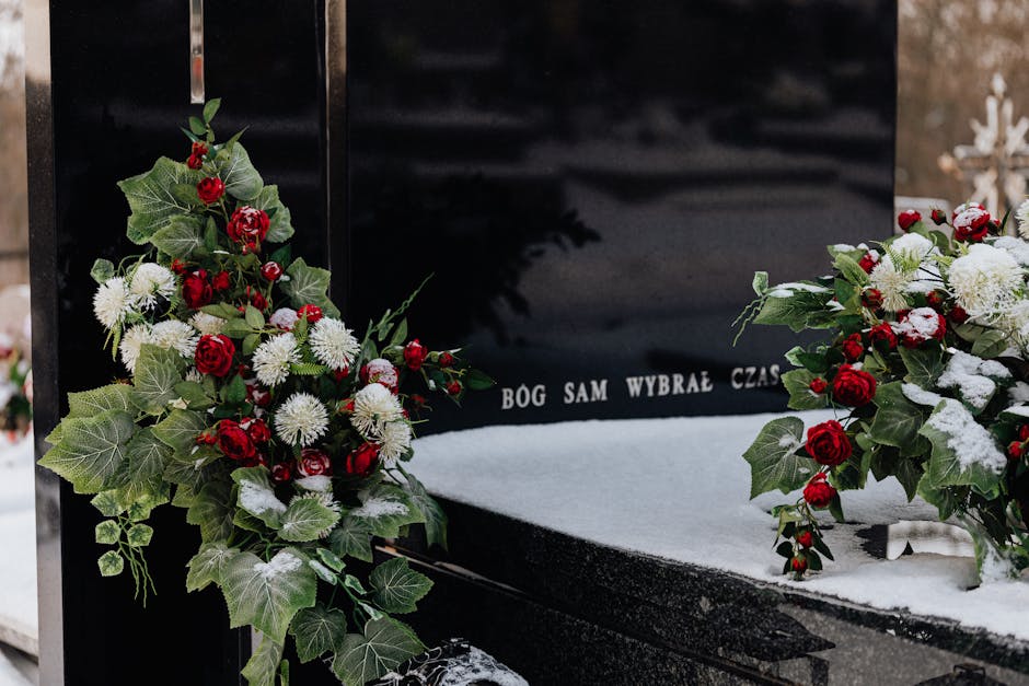 A floral arrangement placed on a black gravestone with the inscription 'BOG SAM WYBRAŁ CZAS', featuring two bouquets of fresh flowers with red roses, white chrysanthemums, and green ivy leaves, some