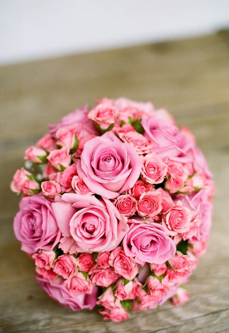 A round bouquet arrangement of fresh pink roses of varying sizes, including large fully bloomed roses and smaller rosebuds. The roses are tightly clustered, showcasing their layered petals and vibrant