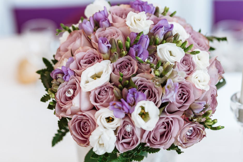 A close-up of a floral bouquet featuring soft pink roses, white lisianthus, and purple freesia, all fresh and vibrant with slightly open petals revealing delicate textures. The arrangement is densely